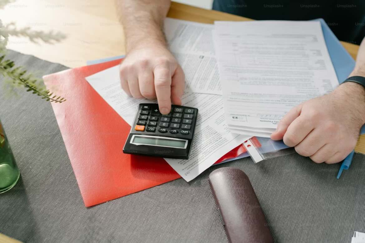 A person using a calculator over top various tax forms.