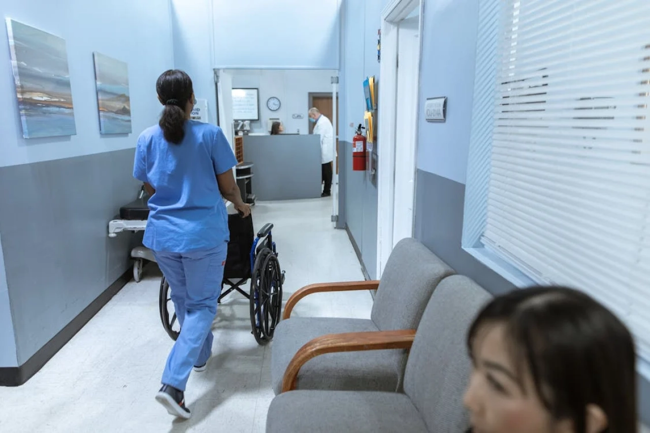 nurse pushing empty wheelchair down hallway in clinic.