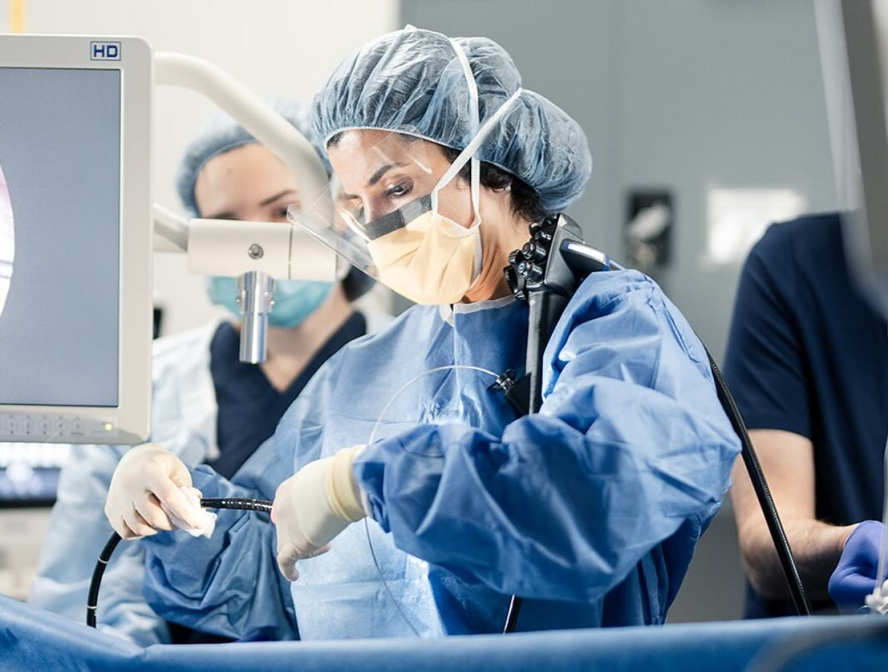 A surgeon in scrubs and a mask performing a procedure in a surgery room.